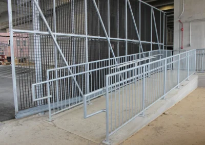 An interior concrete ramp and staircase with metal railings, illuminated by natural light from large windows.