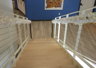 A modern office staircase decorated with colorful tinsel garlands, showcasing wooden steps and sleek metal railings.