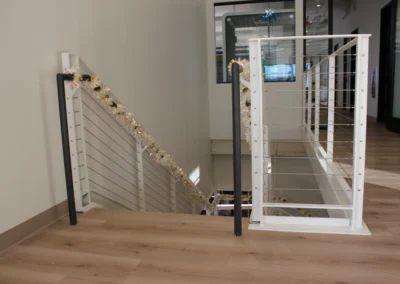 A modern office staircase decorated with colorful tinsel garlands, showcasing wooden steps and sleek metal railings.