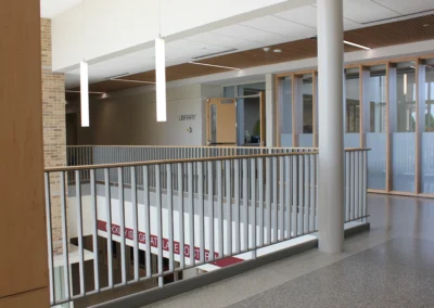 Interior view of a stairwell with gray steps and stainless steel handrails, flanked by red tile and gray block walls. Brightly lit.