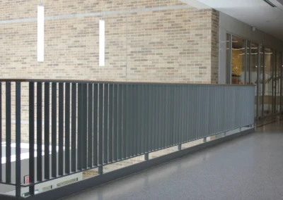 Interior view of a stairwell with gray steps and stainless steel handrails, flanked by red tile and gray block walls. Brightly lit.